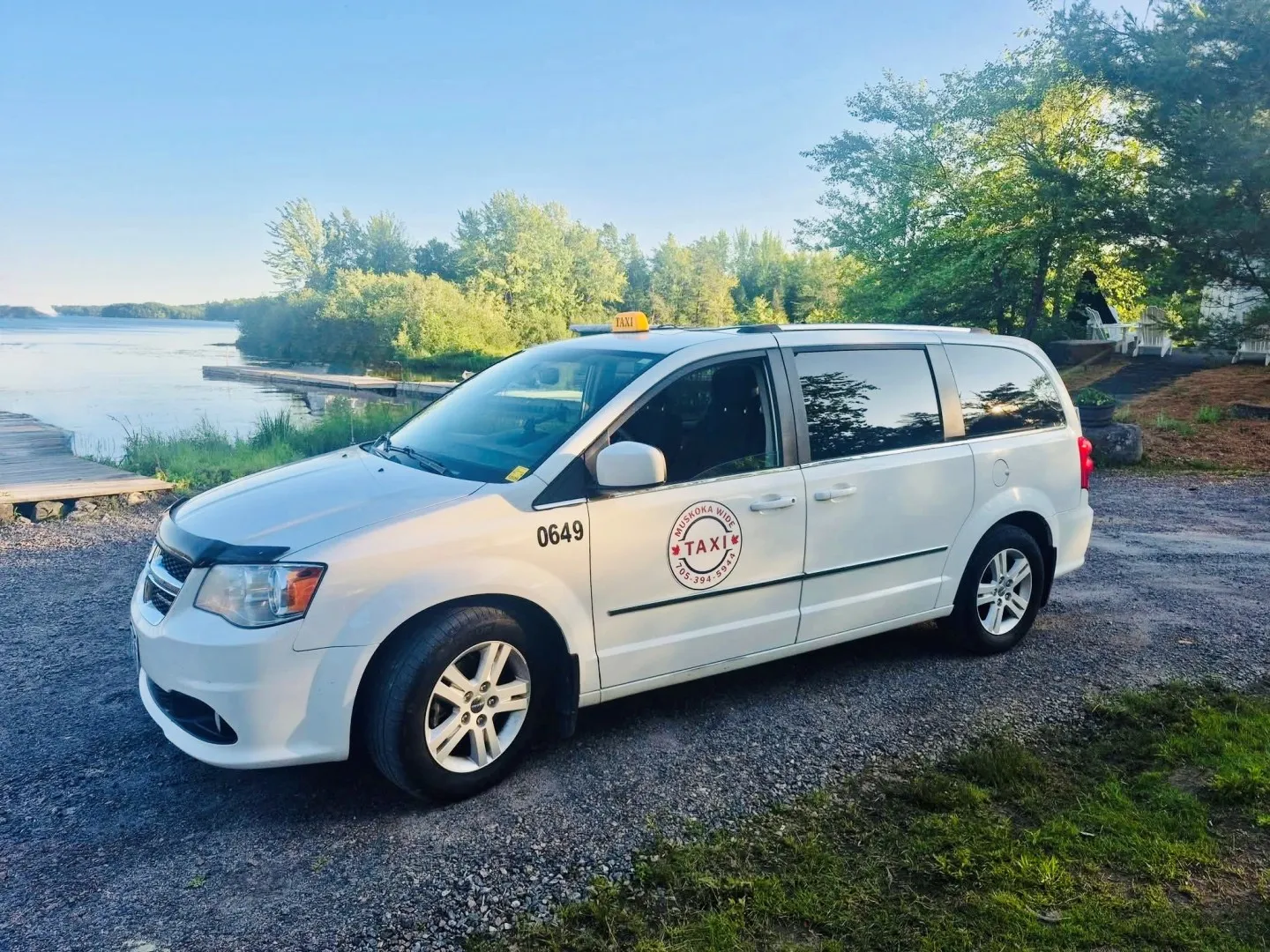 Three Muskoka Wide Taxi white Dodge Grand Caravan minivans parked against Muskoka's Canadian Shield rock face and forest